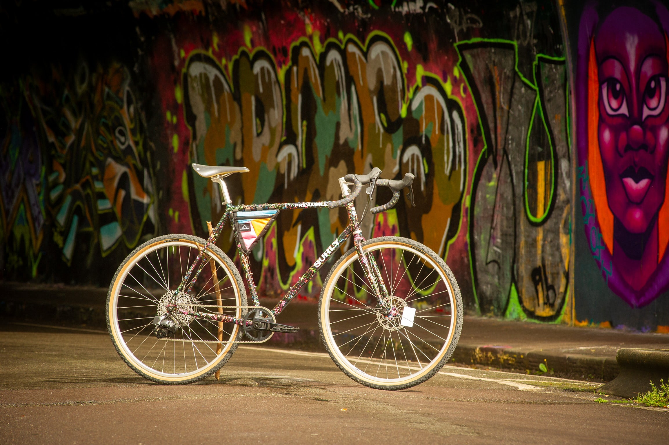 Surly Preamble custom build with custom splatter paint held up by stick on street in tunnel with graffiti