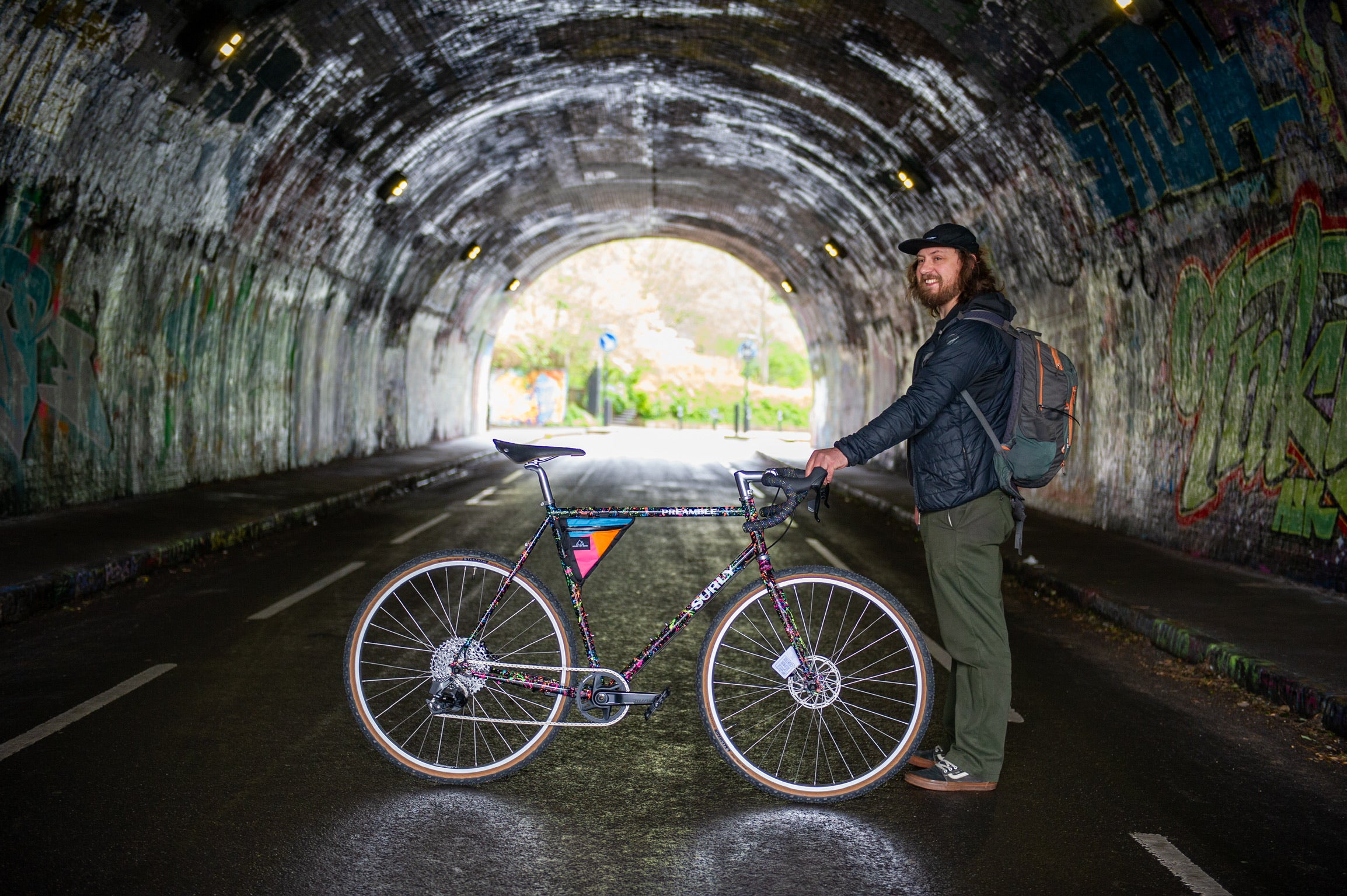 Person smiling while holding custom Surly Preamble with splatter paint in tunnel with graffiti