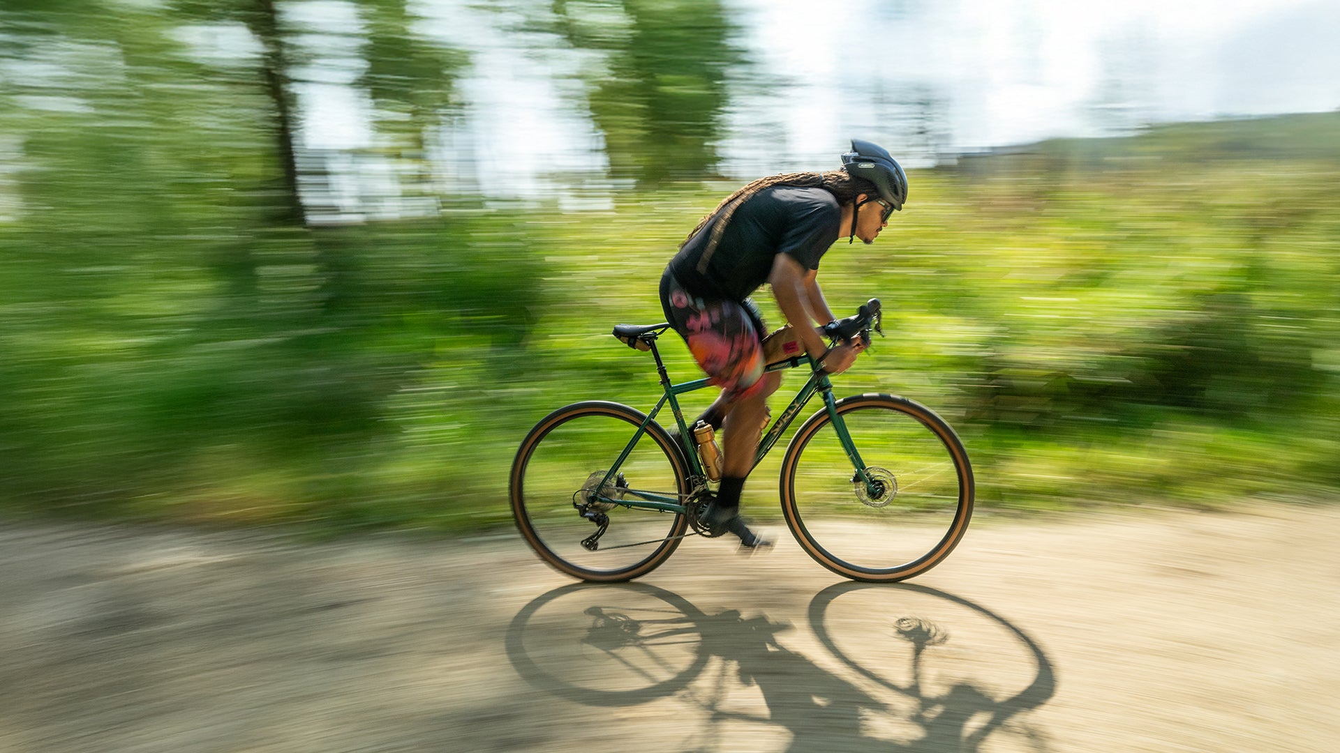 Cyclist riding Surly Straggler bike on gravel road sprinting out of saddle blurry green background